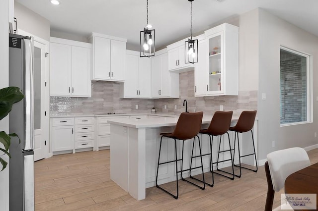 kitchen featuring light hardwood / wood-style floors, a kitchen breakfast bar, stainless steel fridge, and white cabinetry