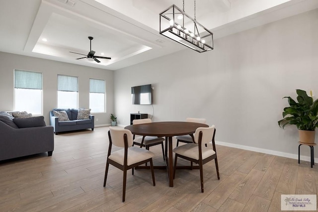 dining area featuring ceiling fan, light hardwood / wood-style floors, and a tray ceiling