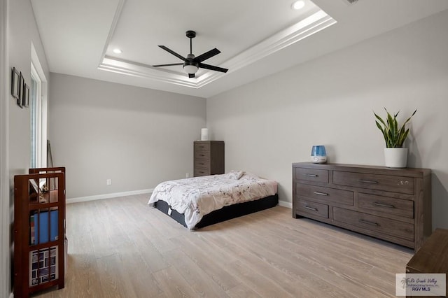 bedroom featuring light wood-type flooring, a raised ceiling, and ceiling fan