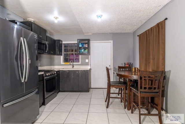 kitchen with appliances with stainless steel finishes, sink, light tile patterned flooring, and a textured ceiling