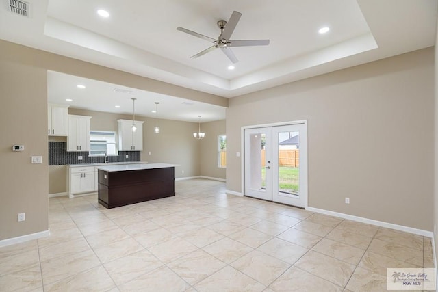 kitchen featuring white cabinets, ceiling fan with notable chandelier, a tray ceiling, decorative light fixtures, and a kitchen island