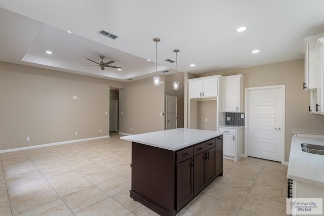 kitchen featuring a tray ceiling, ceiling fan, white cabinets, and a kitchen island