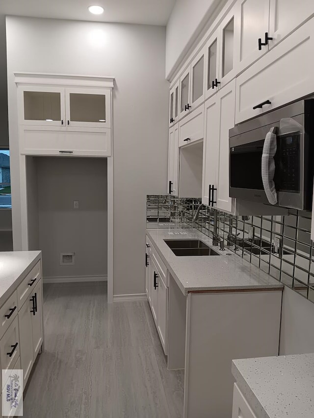 kitchen featuring white cabinetry, sink, light stone countertops, and light wood-type flooring