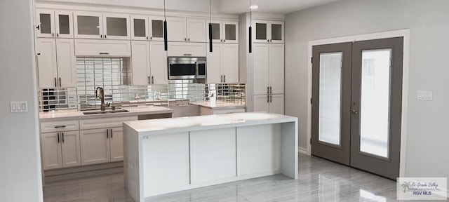 kitchen with sink, a kitchen island, backsplash, pendant lighting, and white cabinets