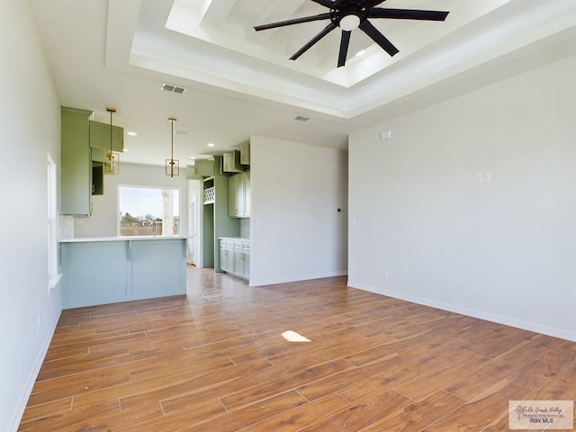 unfurnished living room with a tray ceiling, ceiling fan, and light wood-type flooring