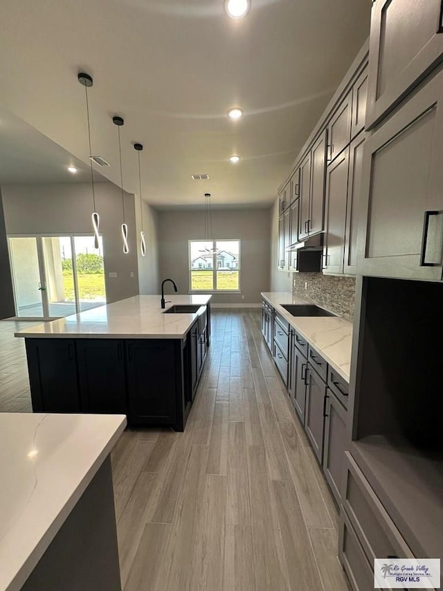 kitchen featuring light stone countertops, light hardwood / wood-style flooring, pendant lighting, black electric cooktop, and decorative backsplash