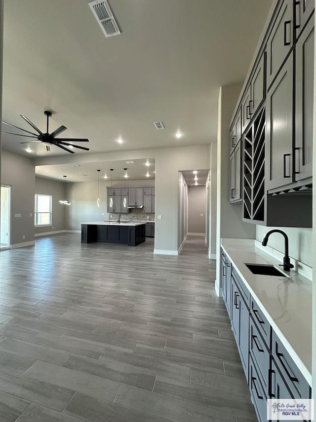 kitchen featuring ceiling fan, sink, light stone countertops, decorative light fixtures, and gray cabinets