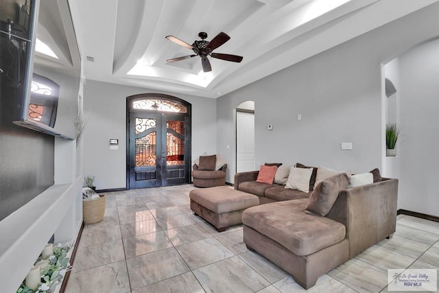 living room featuring arched walkways, a tray ceiling, french doors, and a ceiling fan