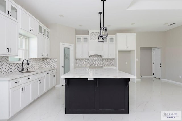 kitchen with white cabinetry, a center island, tasteful backsplash, light stone counters, and decorative light fixtures