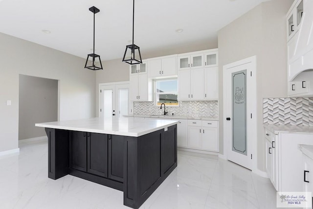 kitchen featuring pendant lighting, backsplash, white cabinets, a spacious island, and sink