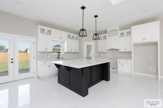 kitchen featuring decorative backsplash, white cabinetry, french doors, and an island with sink