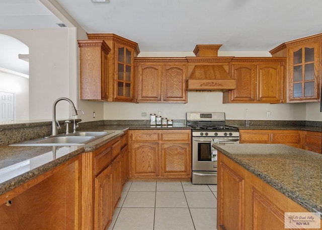 6540 Dockberry Rd, Brownsville, TX 78521 - kitchen with gas stove, custom range hood, brown cabinets, light tile patterned flooring, and dark stone counters
