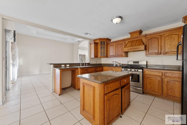 6540 Dockberry Rd, Brownsville, TX 78521 - kitchen with stainless steel range with gas stovetop, light tile patterned floors, brown cabinetry, arched walkways, and a kitchen island
