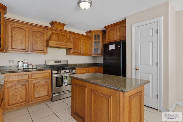 6540 Dockberry Rd, Brownsville, TX 78521 - kitchen with freestanding refrigerator, stainless steel range with gas cooktop, light tile patterned floors, brown cabinets, and glass insert cabinets