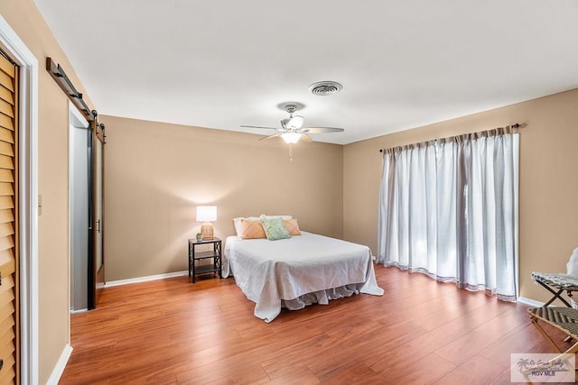 bedroom featuring a barn door, ceiling fan, and hardwood / wood-style flooring