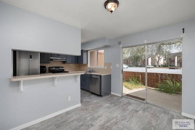 kitchen with a kitchen bar, light countertops, under cabinet range hood, light wood-style floors, and stainless steel appliances