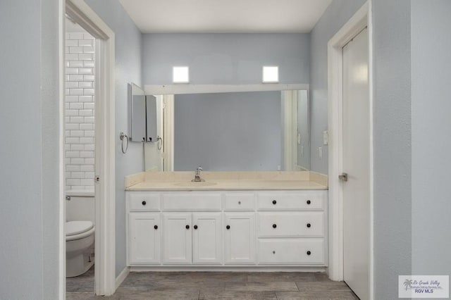 bathroom featuring toilet, baseboards, wood finished floors, and vanity