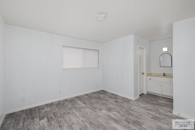 unfurnished bedroom featuring connected bathroom, baseboards, a sink, and wood finished floors