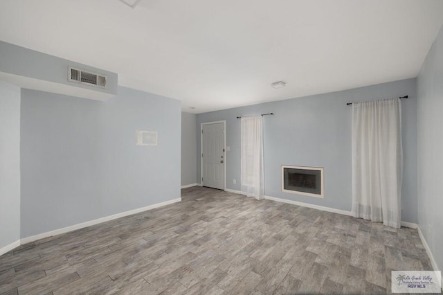 unfurnished living room featuring baseboards, visible vents, wood finished floors, and a fireplace