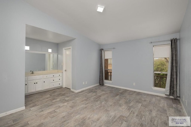 unfurnished bedroom featuring a sink, ensuite bath, light wood-style flooring, baseboards, and lofted ceiling