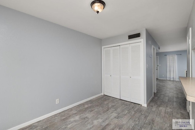 unfurnished bedroom with baseboards, visible vents, wood finished floors, and a closet