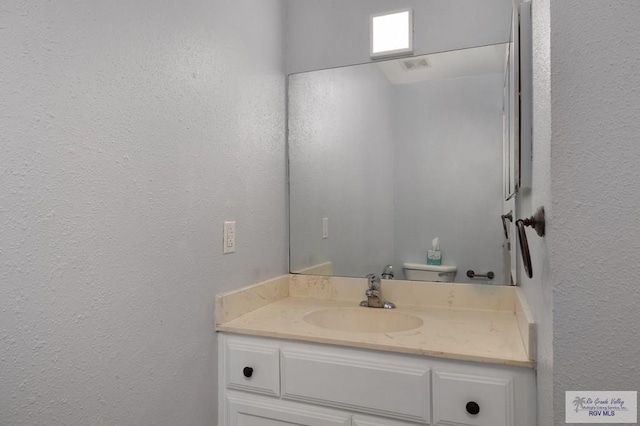 bathroom featuring vanity, a textured wall, and toilet