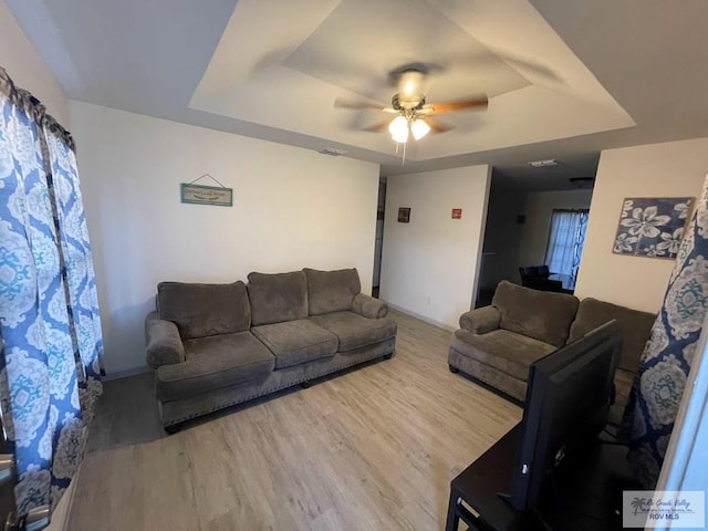 living room with ceiling fan, a tray ceiling, and hardwood / wood-style floors