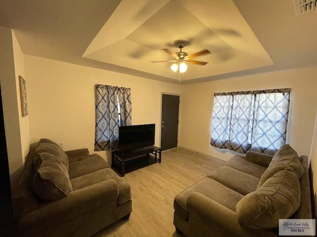 living room featuring ceiling fan, a raised ceiling, and light hardwood / wood-style flooring