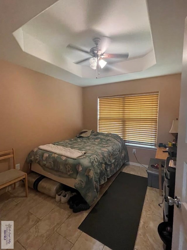 bedroom featuring ceiling fan, light tile patterned floors, and a tray ceiling