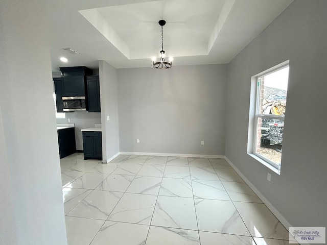 unfurnished dining area with a notable chandelier and a raised ceiling