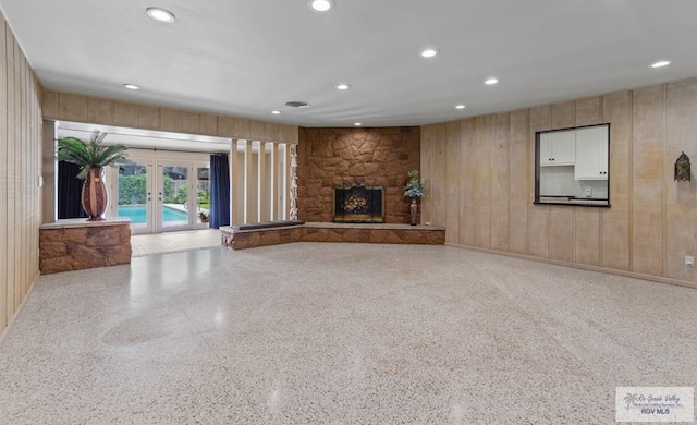 509 Lake Dr, Harlingen, TX 78550 - unfurnished living room with speckled floor, recessed lighting, french doors, a stone fireplace, and wooden walls