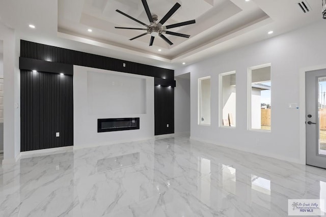 unfurnished living room with marble finish floor, visible vents, a raised ceiling, and a glass covered fireplace