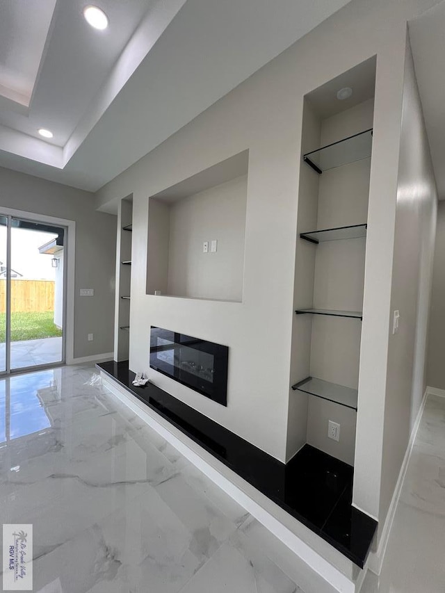 unfurnished living room featuring recessed lighting, baseboards, built in features, marble finish floor, and a glass covered fireplace