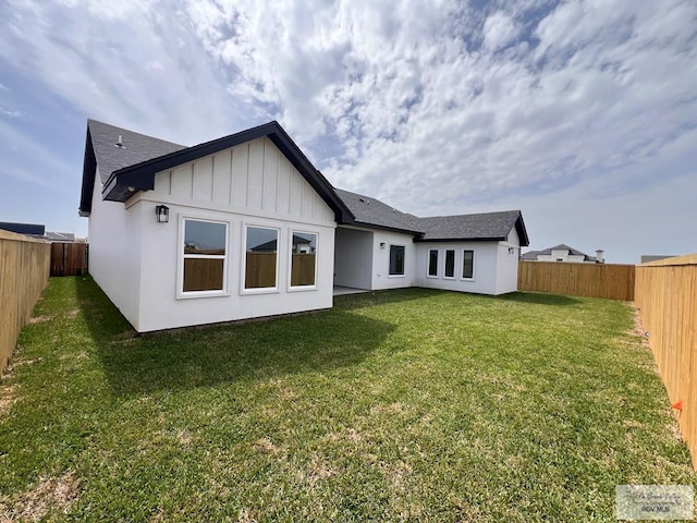 back of house with board and batten siding, a fenced backyard, and a yard