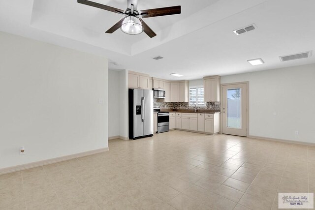 kitchen featuring ceiling fan, sink, a raised ceiling, backsplash, and appliances with stainless steel finishes