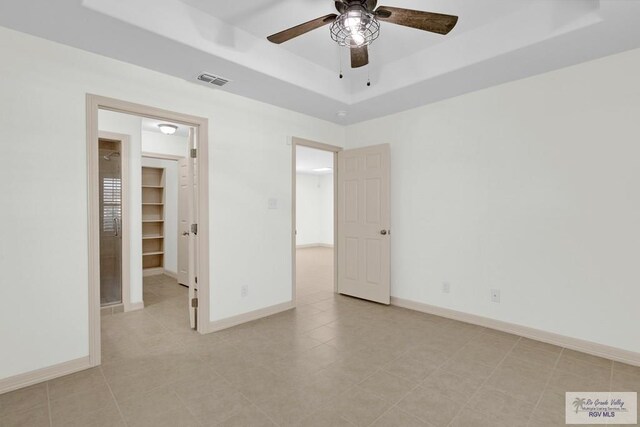 unfurnished bedroom featuring a spacious closet, ceiling fan, a raised ceiling, a closet, and light tile patterned flooring