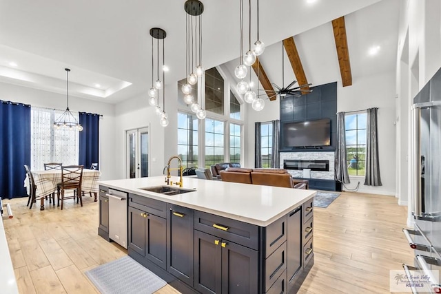 kitchen featuring high vaulted ceiling, hanging light fixtures, sink, an island with sink, and light hardwood / wood-style floors