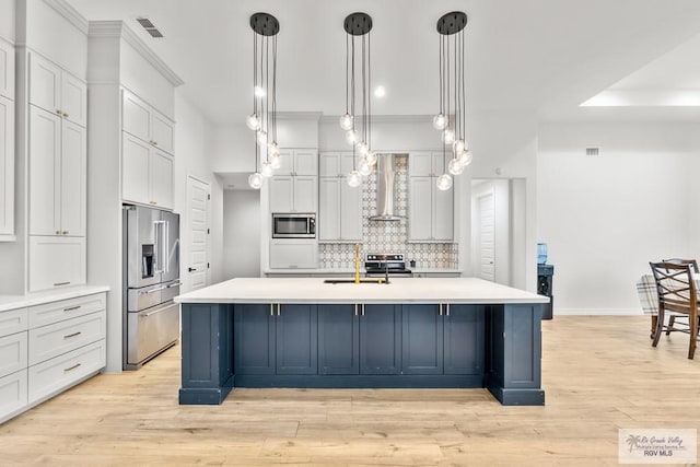 kitchen with pendant lighting, a large island, wall chimney range hood, and stainless steel appliances