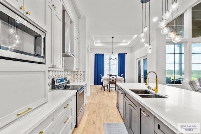 kitchen featuring a tray ceiling, stainless steel appliances, decorative light fixtures, and light wood-type flooring