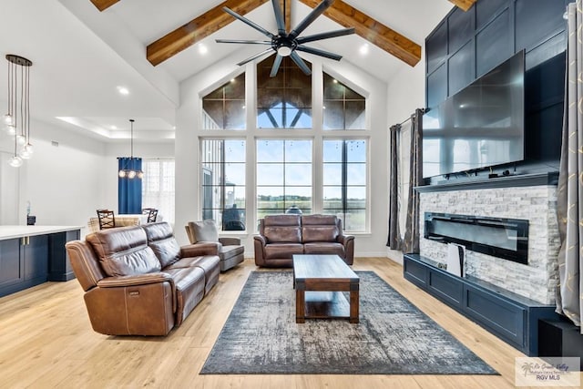 living room featuring a stone fireplace, beamed ceiling, high vaulted ceiling, ceiling fan with notable chandelier, and light wood-type flooring