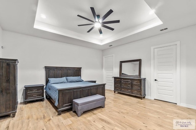 bedroom featuring ceiling fan, light hardwood / wood-style floors, and a raised ceiling