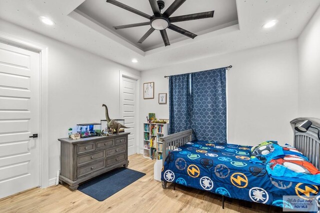 bedroom with a tray ceiling, ceiling fan, and light hardwood / wood-style flooring