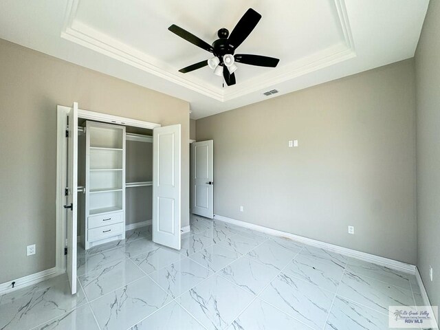 unfurnished bedroom with a raised ceiling, ceiling fan, and a closet