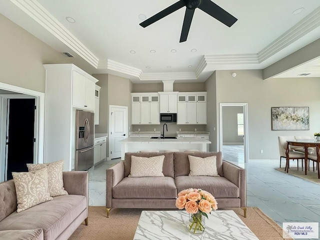 living room featuring a raised ceiling, ceiling fan, and sink