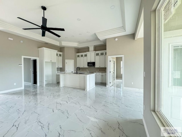 kitchen with white cabinetry, sink, ceiling fan, a towering ceiling, and an island with sink