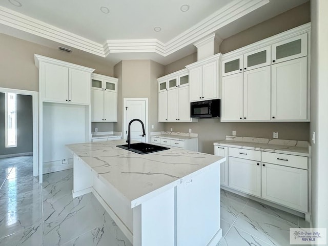 kitchen featuring light stone counters, ornamental molding, a kitchen island with sink, sink, and white cabinets