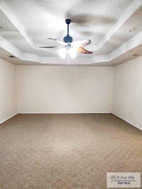 carpeted spare room featuring a textured ceiling, a tray ceiling, and ceiling fan