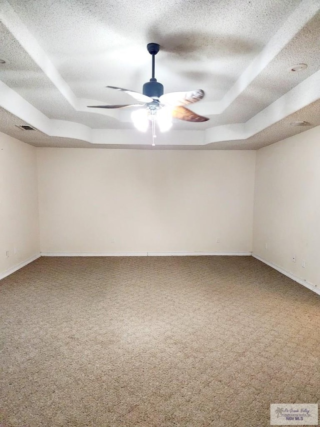 spare room with a raised ceiling, ceiling fan, carpet flooring, and a textured ceiling