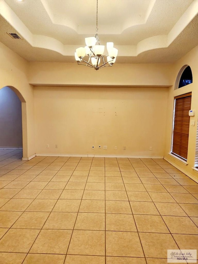 spare room with a tray ceiling, light tile patterned floors, a textured ceiling, and a notable chandelier