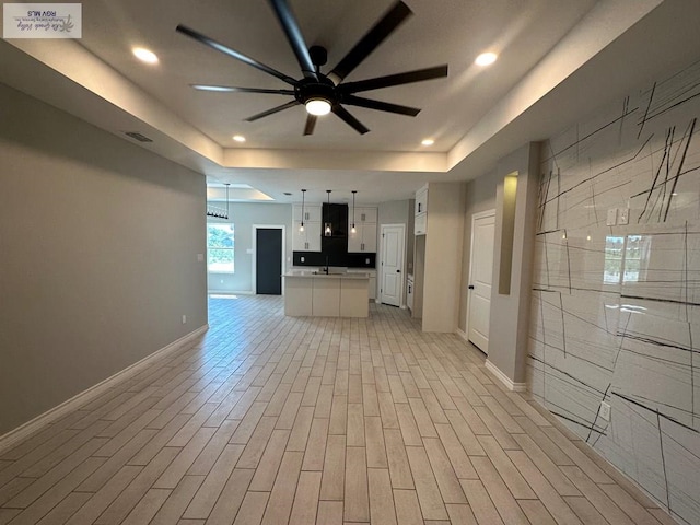 unfurnished living room featuring ceiling fan, recessed lighting, baseboards, light wood-type flooring, and a raised ceiling